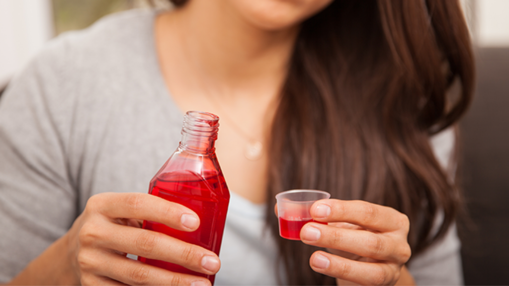 An LGBTQ person pouring cough syrup with DXM into a small cup.