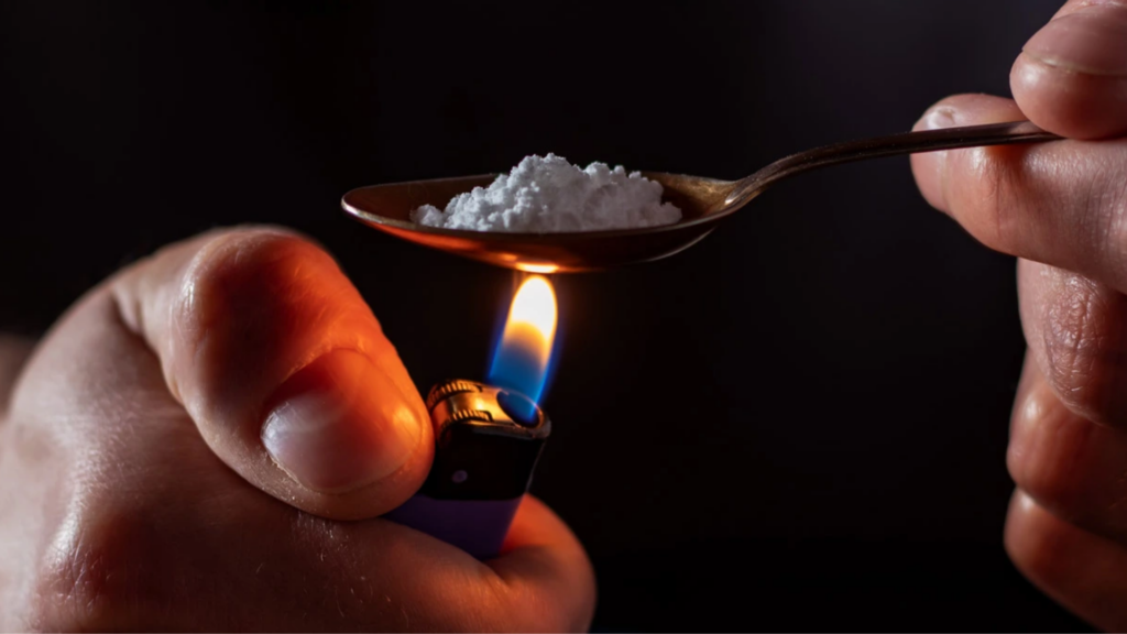 A hand, lighter and spoon with cocaine that someone is about to freebase