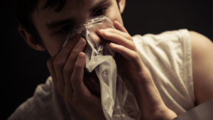 gay person engaging in huffing behavior with a plastic bag, highlighting dangers of substance abuse