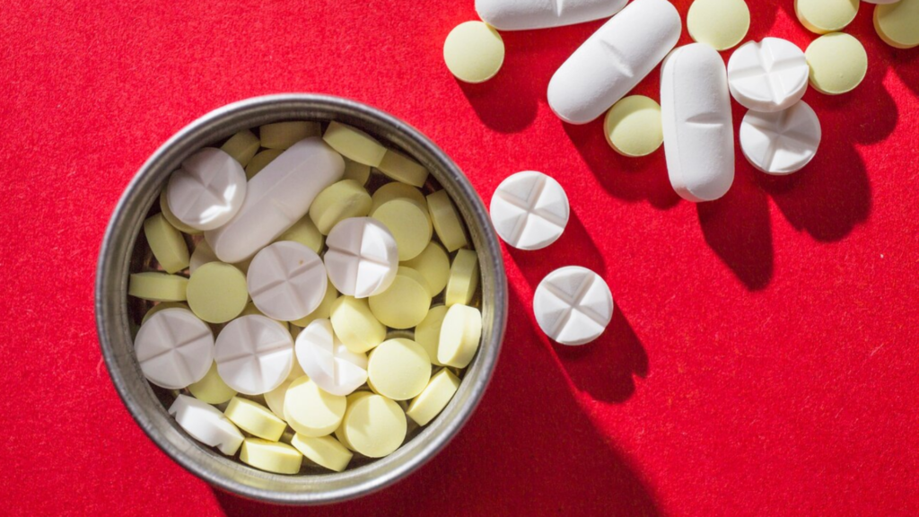 A close-up of various pills on a red background, representing the discussion about what is fentanyl and its harmful effects when misused.