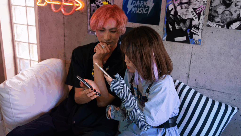Two queer friends, having fun while using their phones in a sober space.