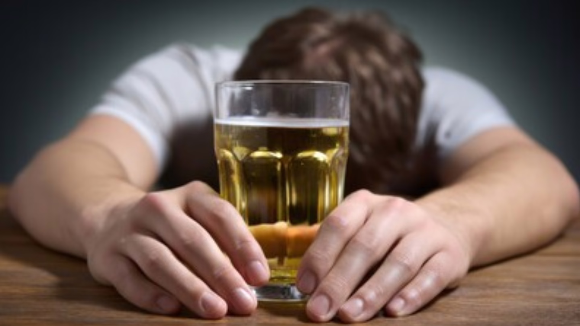 A person holding a glass of beer with head down on the table.